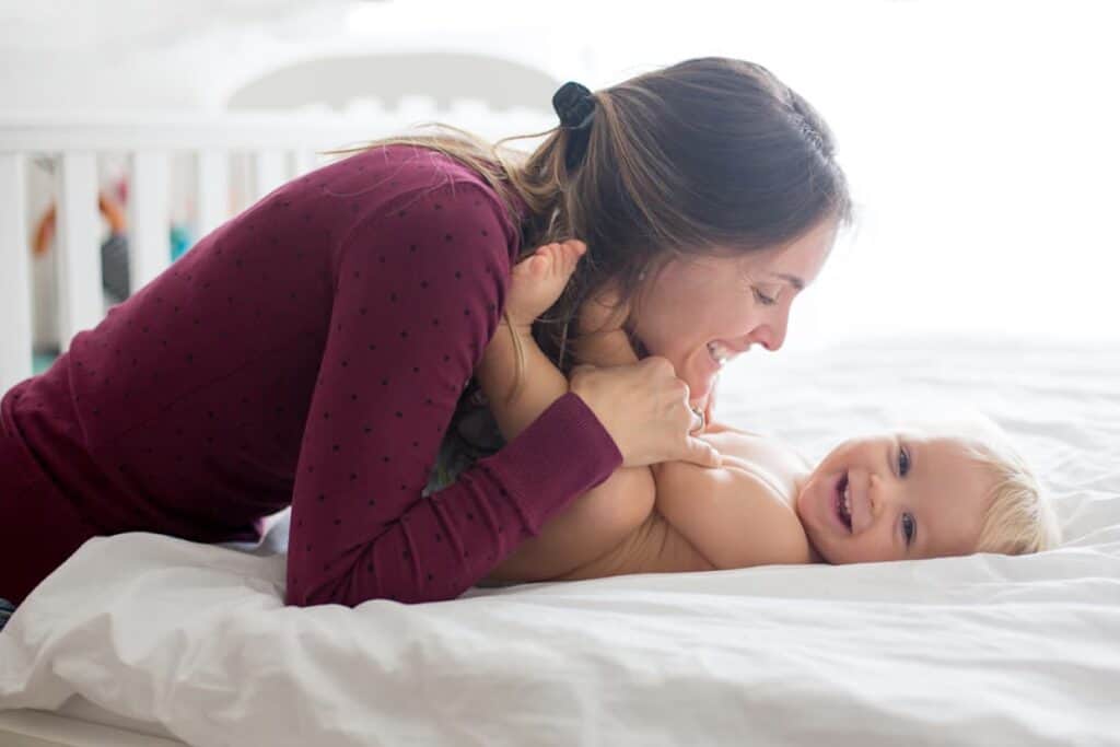 Young mom hugging her baby in sunny bedroom.